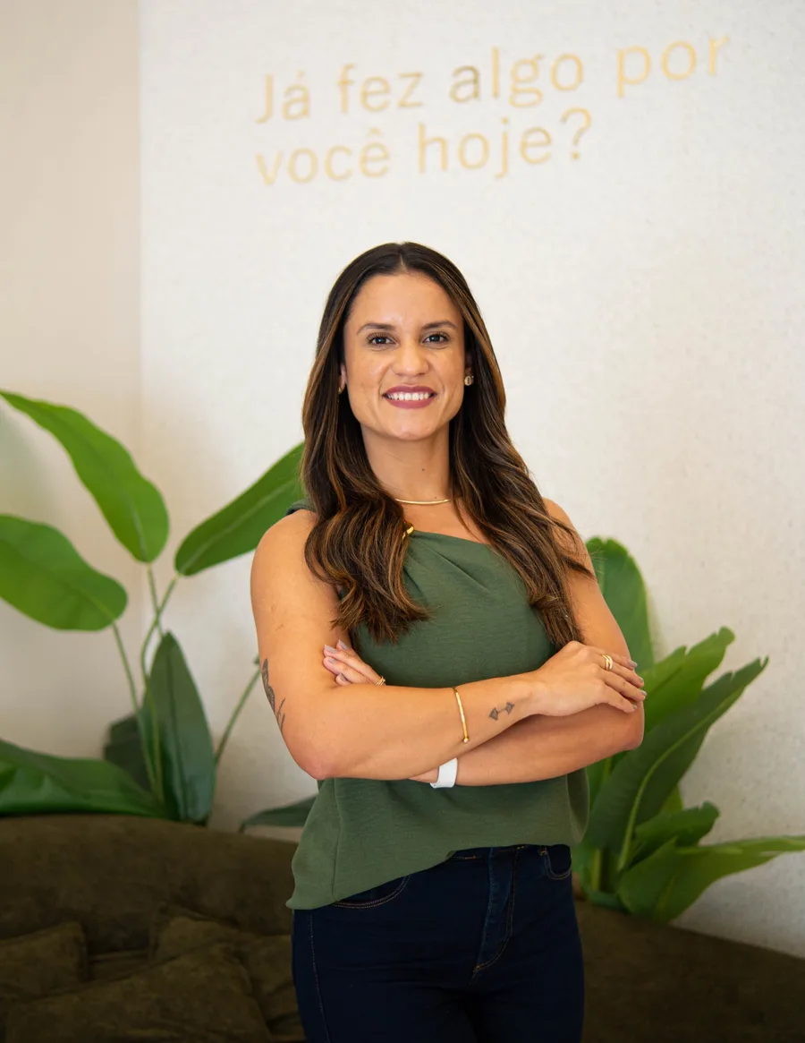 Mariana Costa, nutricionista em Maricá, sorrindo de braços cruzados no consultório em Itaipuaçu