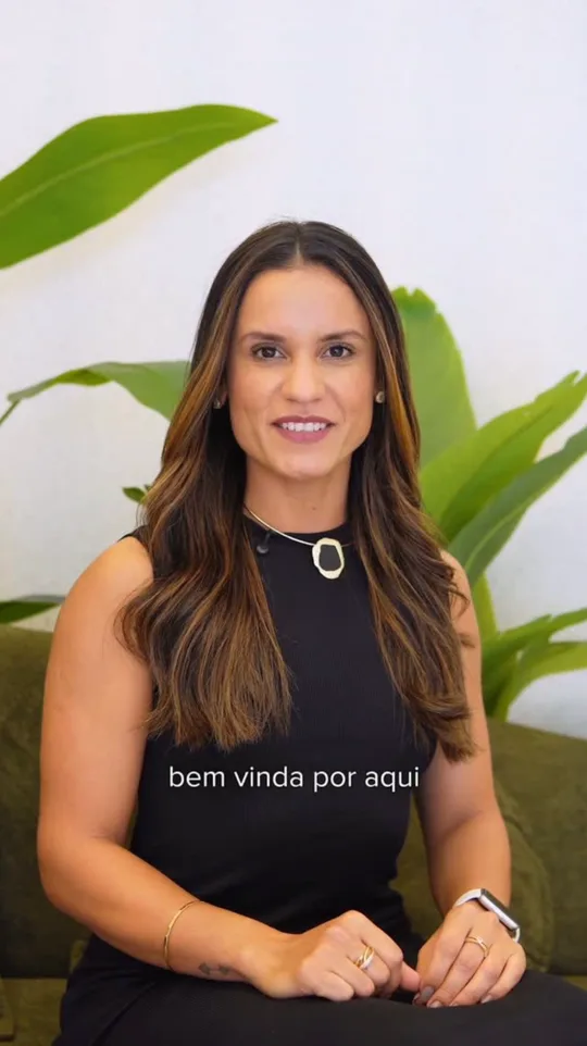 Mariana Costa sentada em frente a plantas, gravando o vídeo de boas-vindas